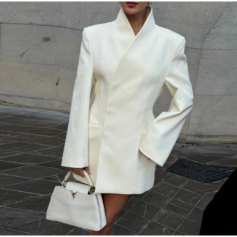 Person wearing a white coat holding a matching handbag on a stone pavement.